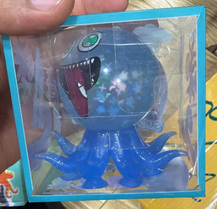 Original supplier photo: Blue octopus character squeeze toy with star details and a cartoon face in a blue-edged clear box